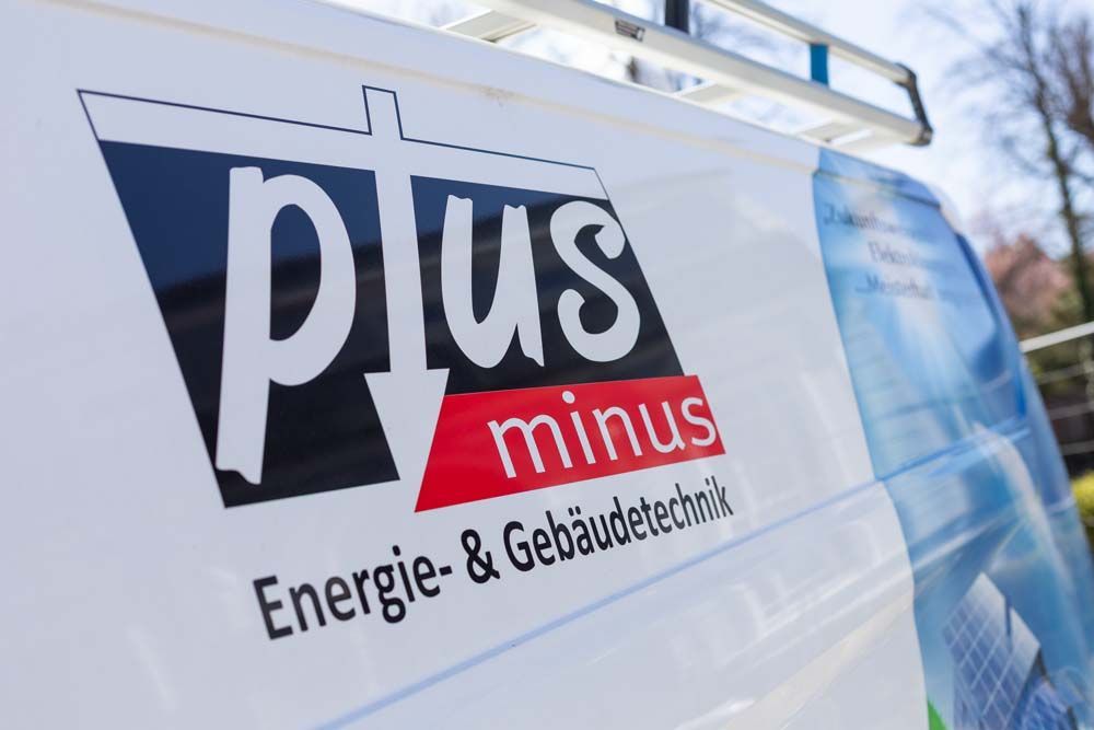 Weißer Lieferwagen mit „plus minus Energie- & Gebäudetechnik“-Logo in Schwarz, Rot und Weiß; im Freien geparkt.
