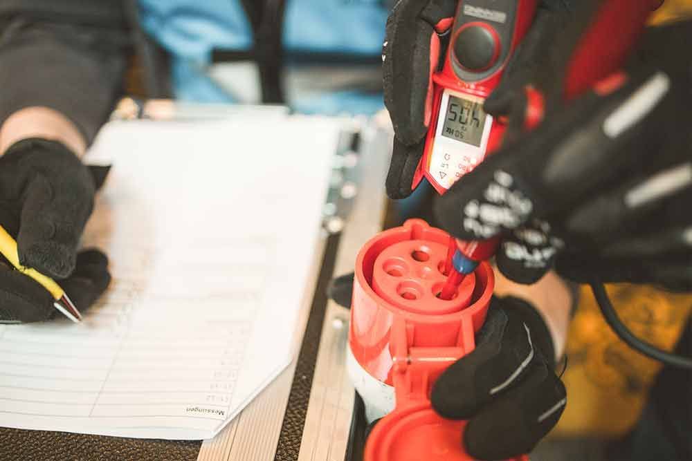 Eine Person schreibt auf ein Klemmbrett, während sie eine rote Steckdose in der Hand hält.