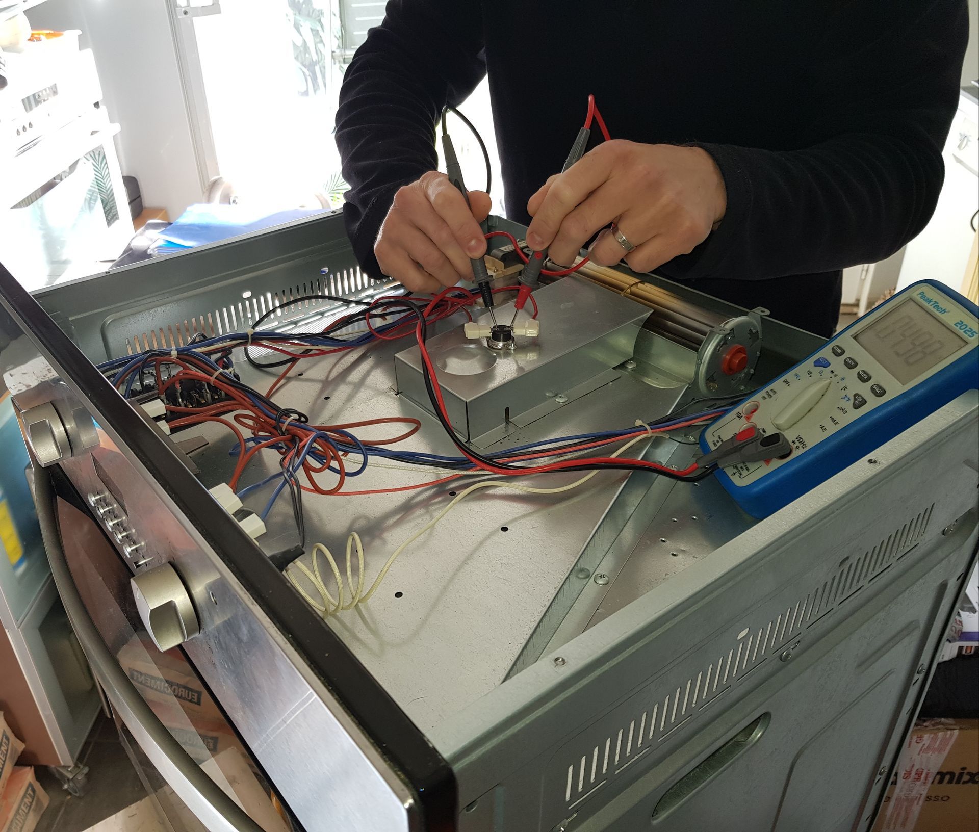 Une personne teste le câblage à l'intérieur d'un four à l'aide d'un multimètre.