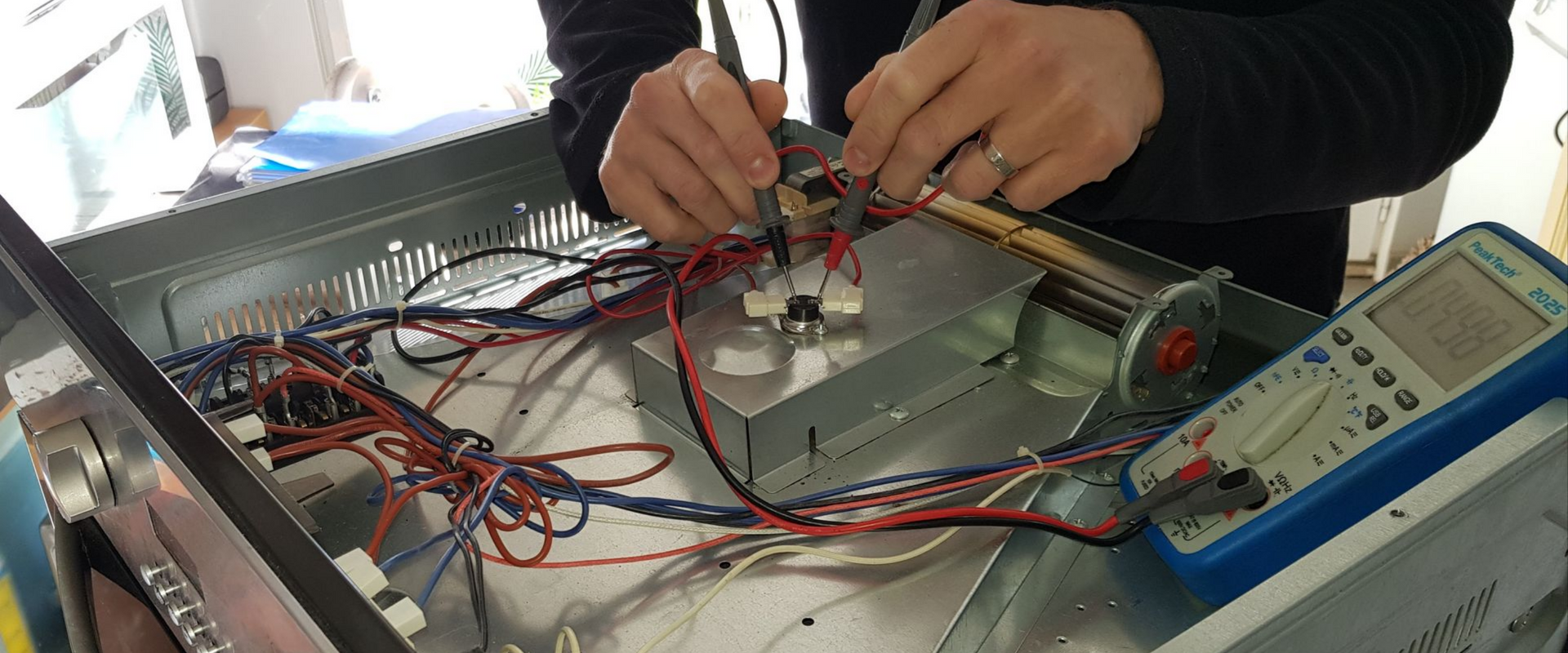 Personne travaillant sur le câblage à l'intérieur d'une boîte métallique, à l'aide d'un multimètre.