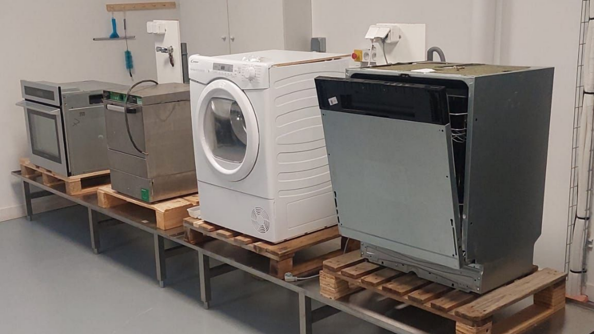 Rangée d'appareils électroménagers sur palettes, comprenant un four, un lave-vaisselle, une machine à laver et un lave-vaisselle dans un laboratoire.