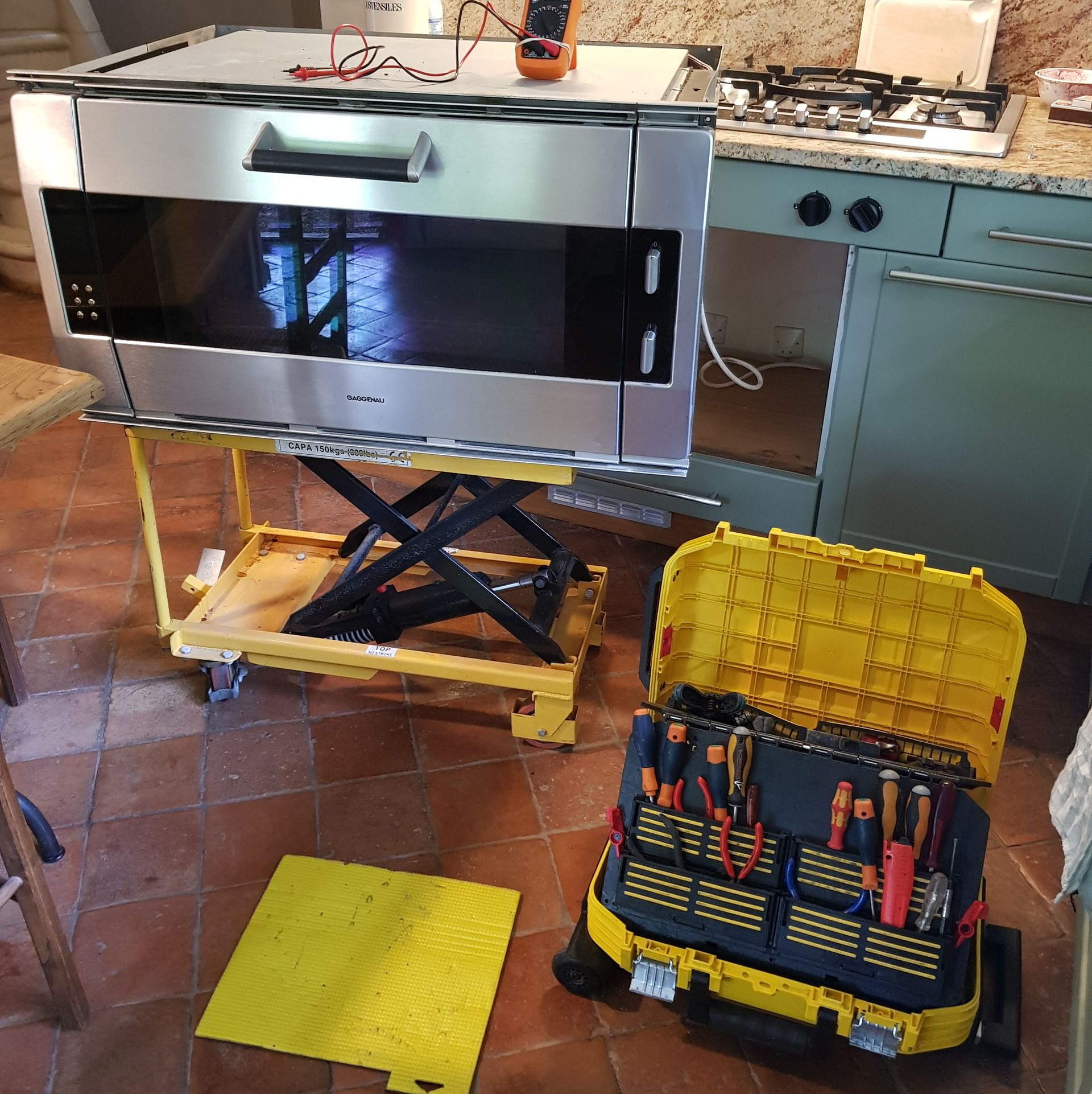 Four sur un élévateur avec une boîte à outils. Un électricien teste le four dans une cuisine.