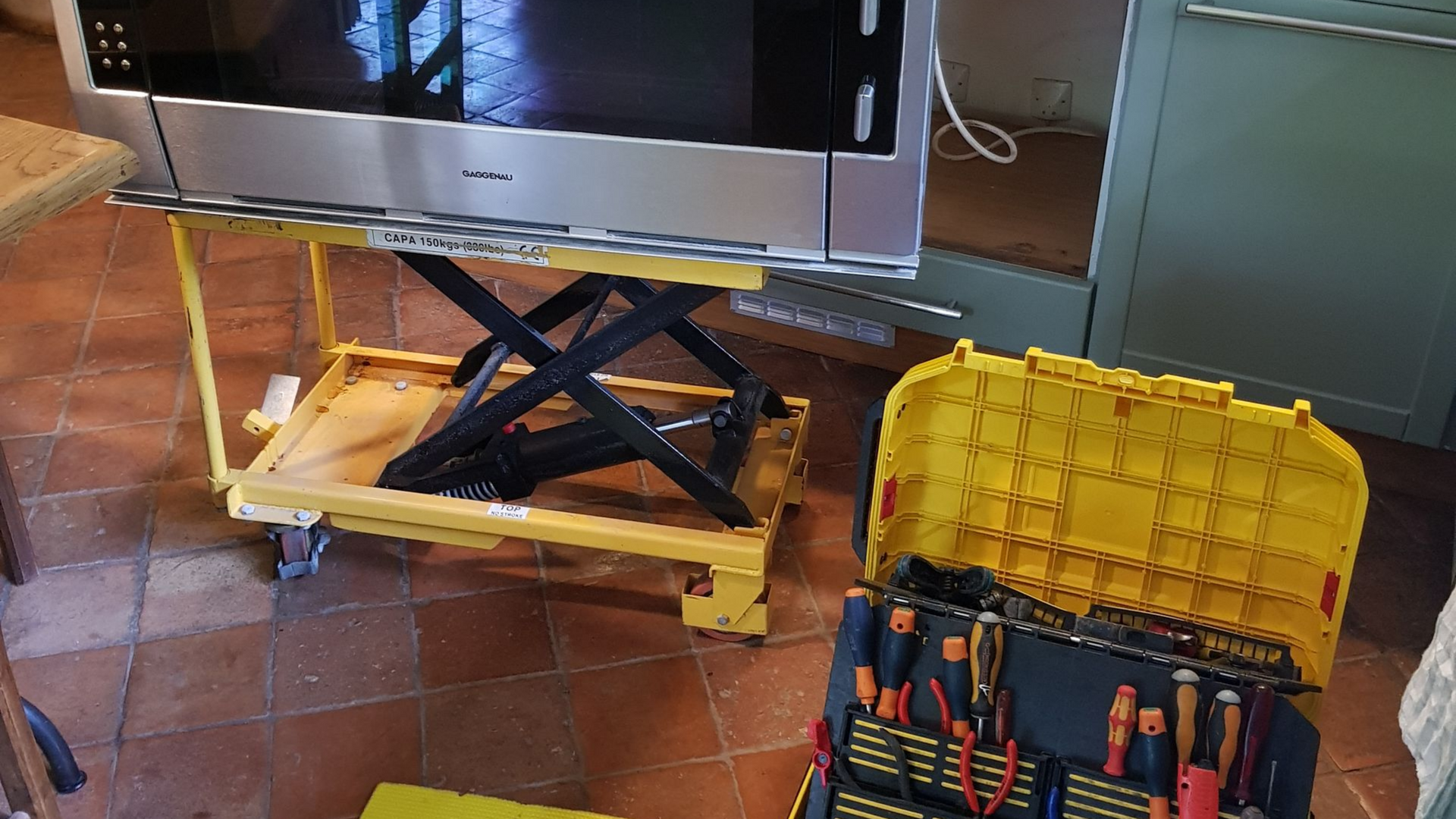 Un téléviseur sur un chariot élévateur jaune, avec une boîte à outils jaune au sol.