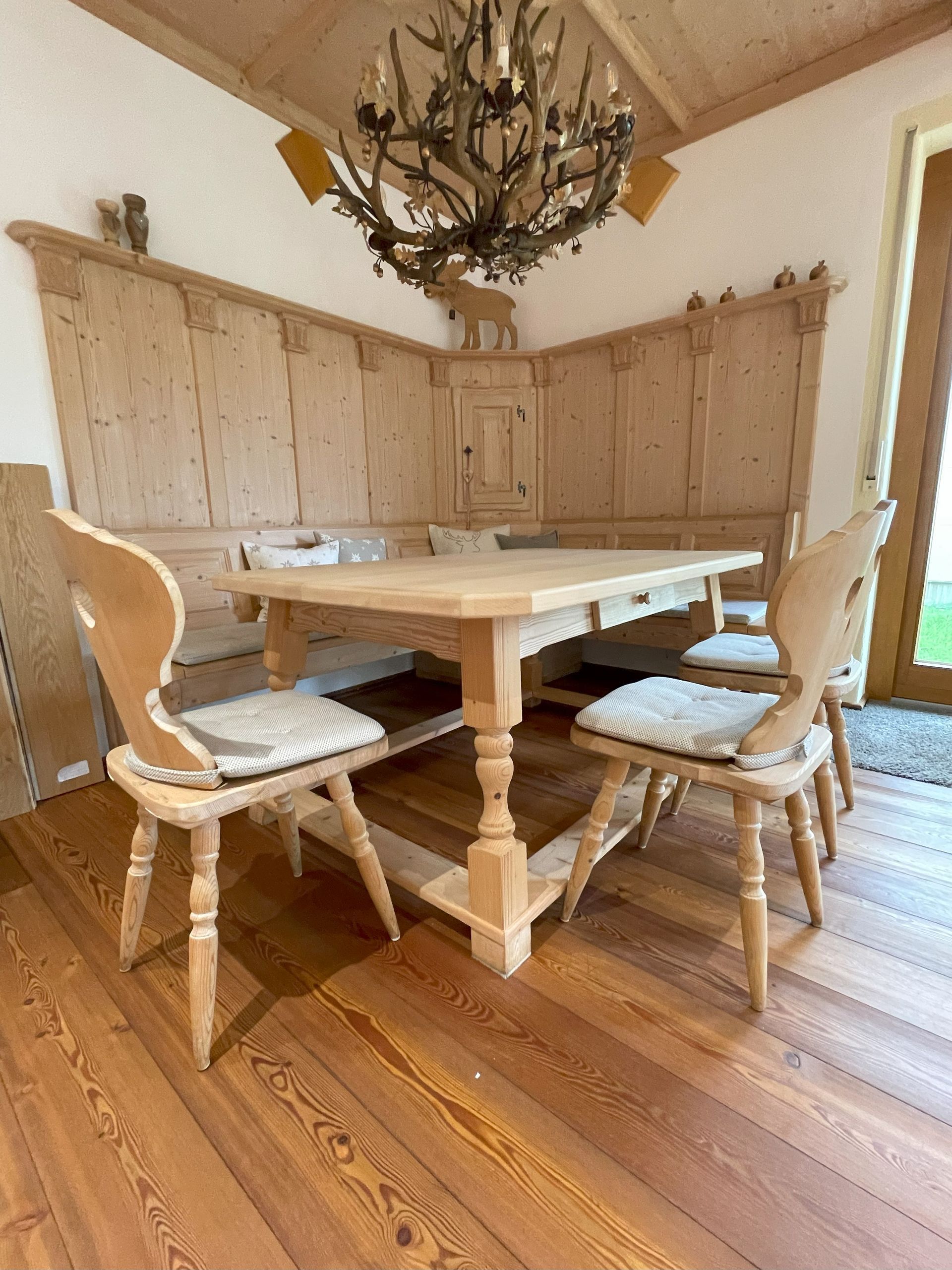 Esstischgarnitur aus Holz in einem rustikalen Raum mit Eckbank, Stühlen und Kronleuchter.