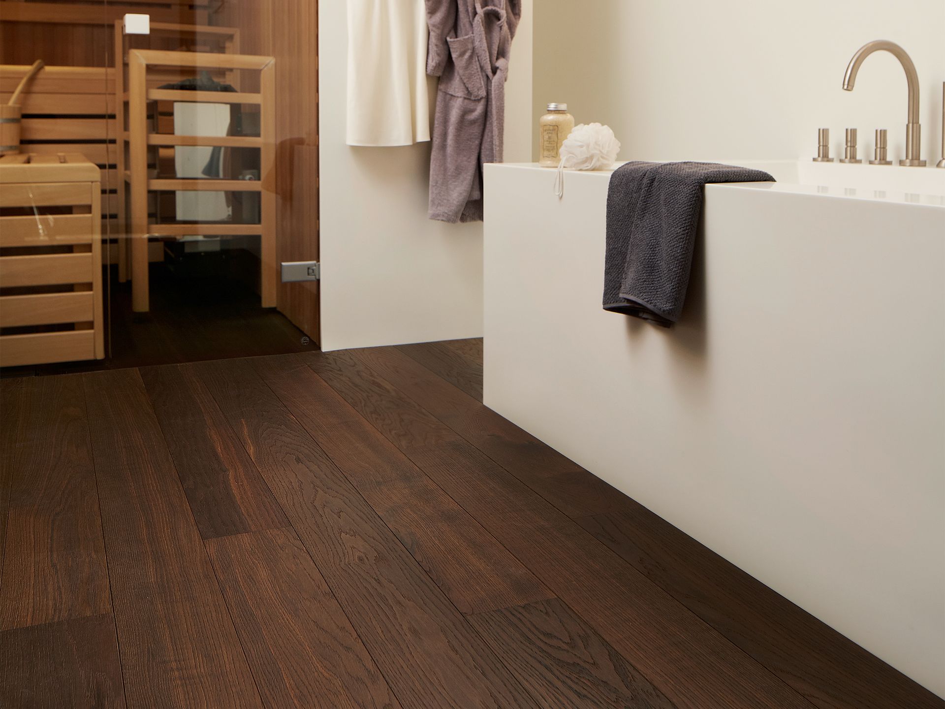 Dunkler Holzboden in einem Badezimmer mit einer weißen Badewanne und einer im Hintergrund sichtbaren Sauna.