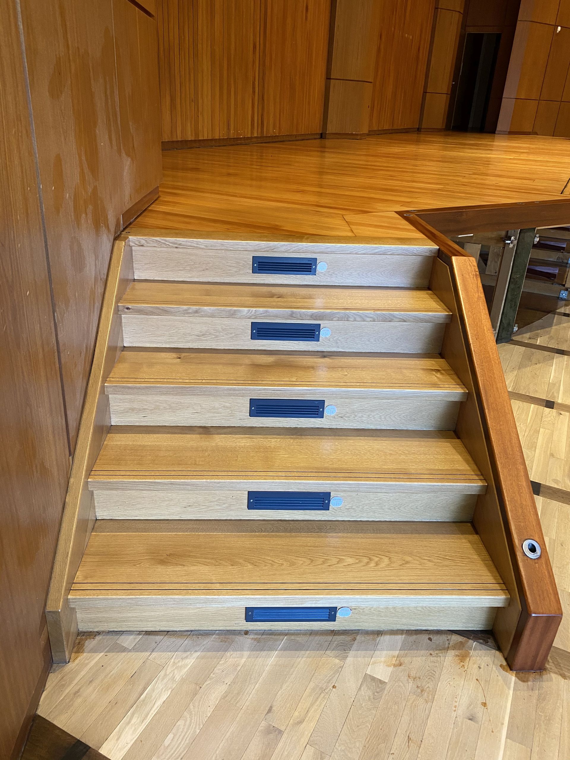 Holztreppe mit blauen Einlegedetails, die nach oben in einen holzgetäfelten Raum führt.