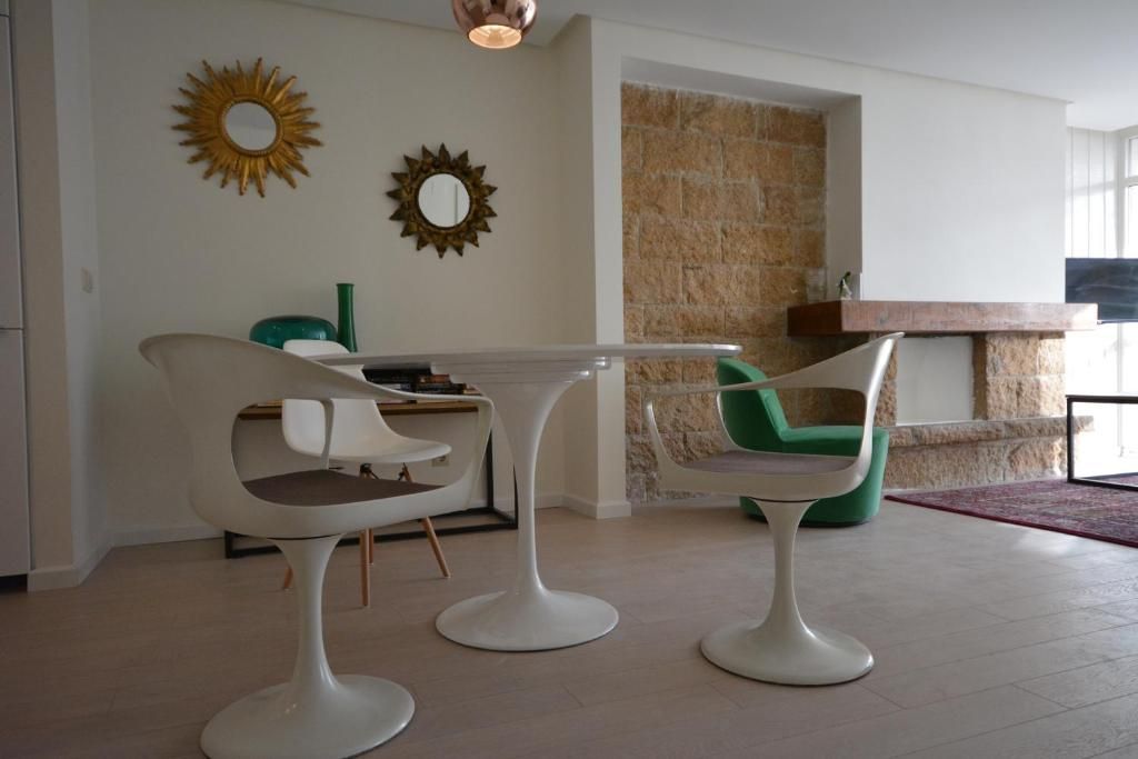 Área de comedor con mesa y sillas de tulipán blanco, chimenea de piedra y espejos dorados con efecto rayos de sol.