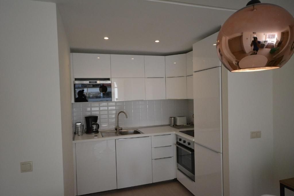 Cocina blanca con armarios, microondas, fregadero y horno. Lámpara colgante de cobre.