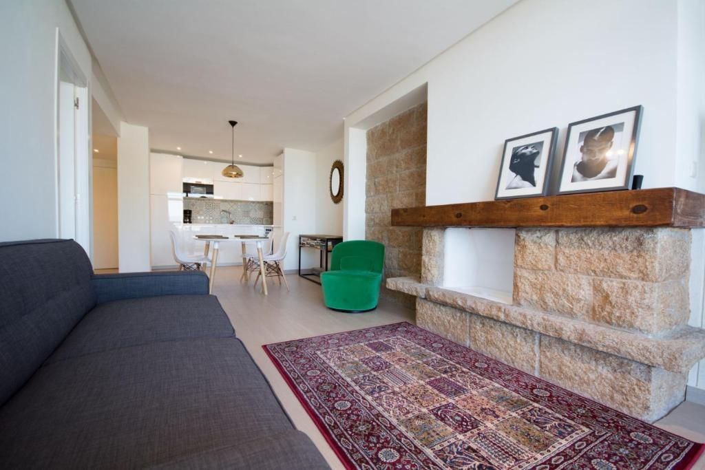 Salón con chimenea, sofá, alfombra y cocina abierta al fondo.