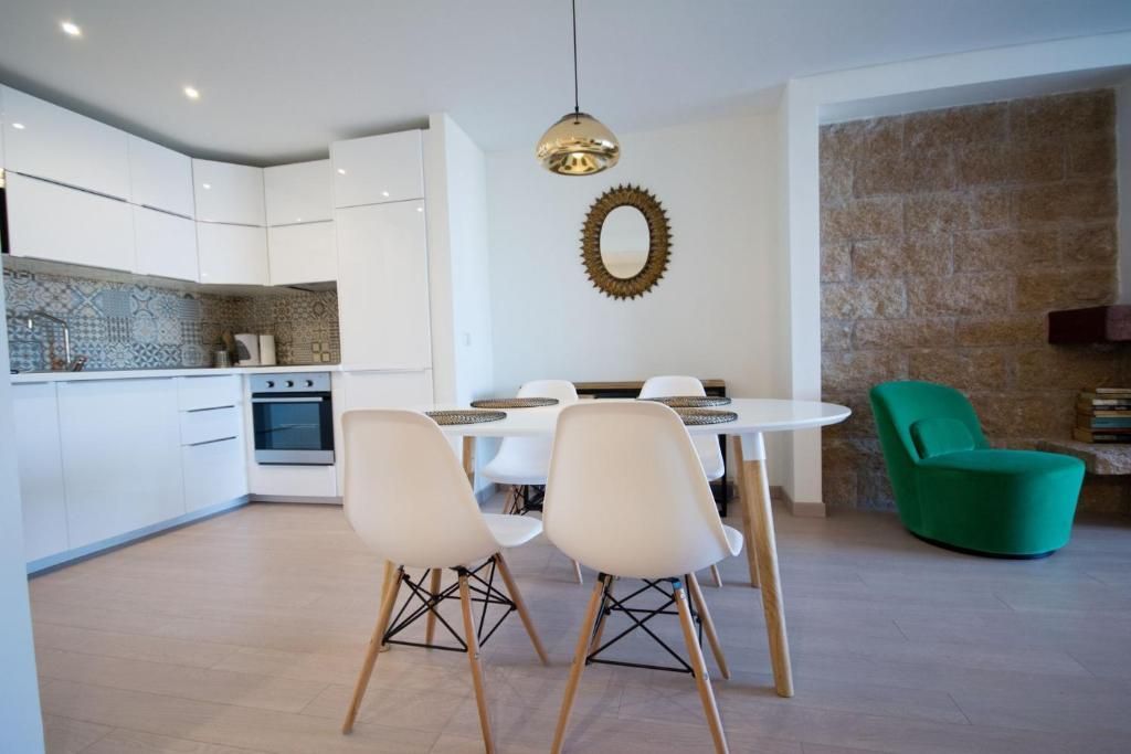 Moderna cocina abierta y comedor con gabinetes blancos, mesa redonda y sillón verde.