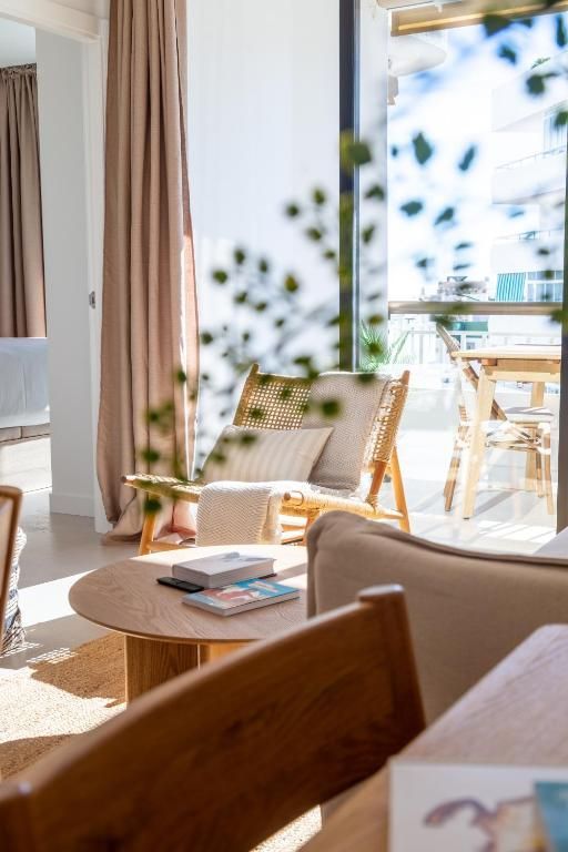 Balcón con mesa redonda de madera, sillas y pantalla de lámpara tejida. Vistas a la zona verde y al mar.