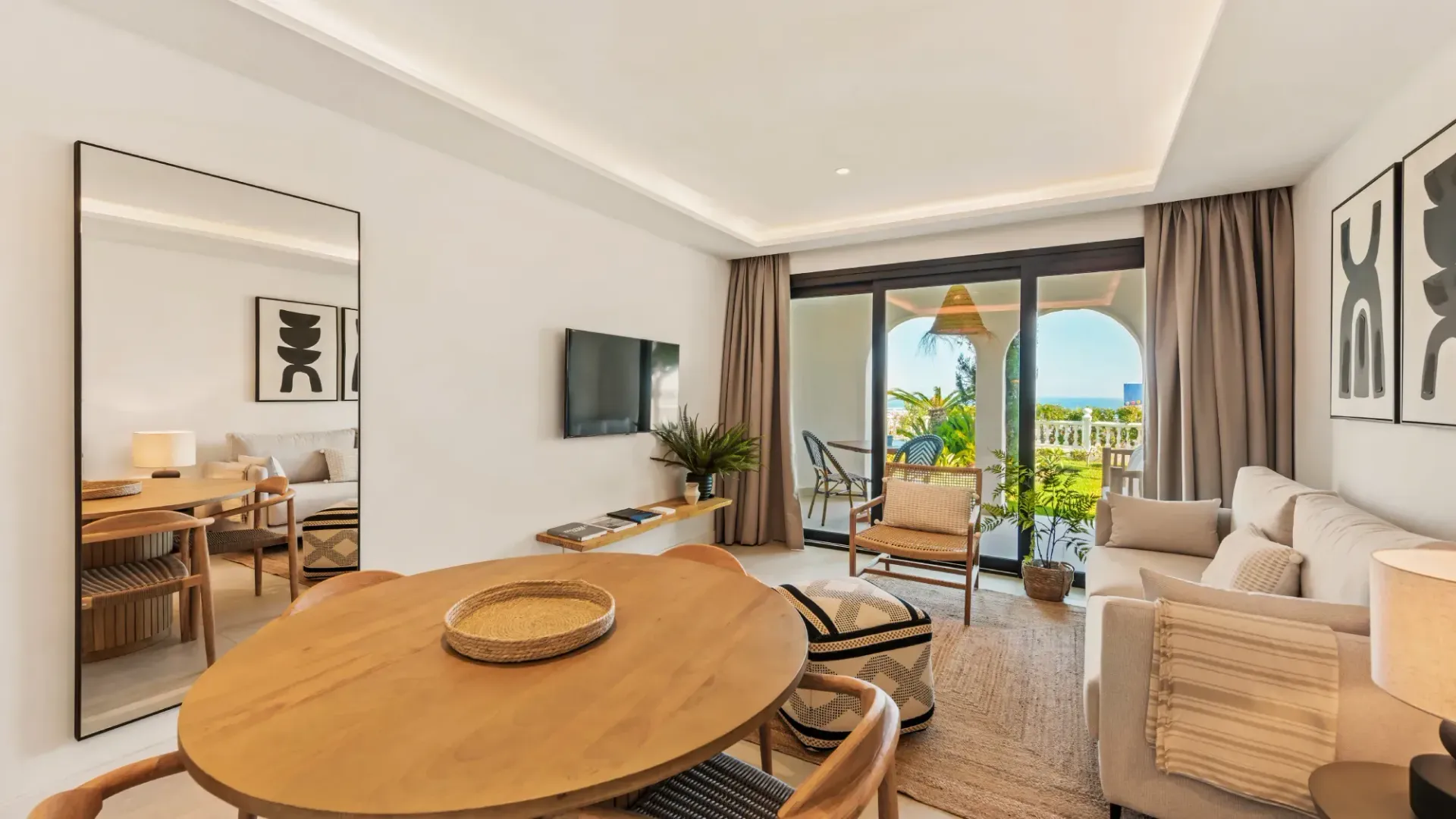 Luminoso salón con balcón abierto, mesa de madera y sofá beige.