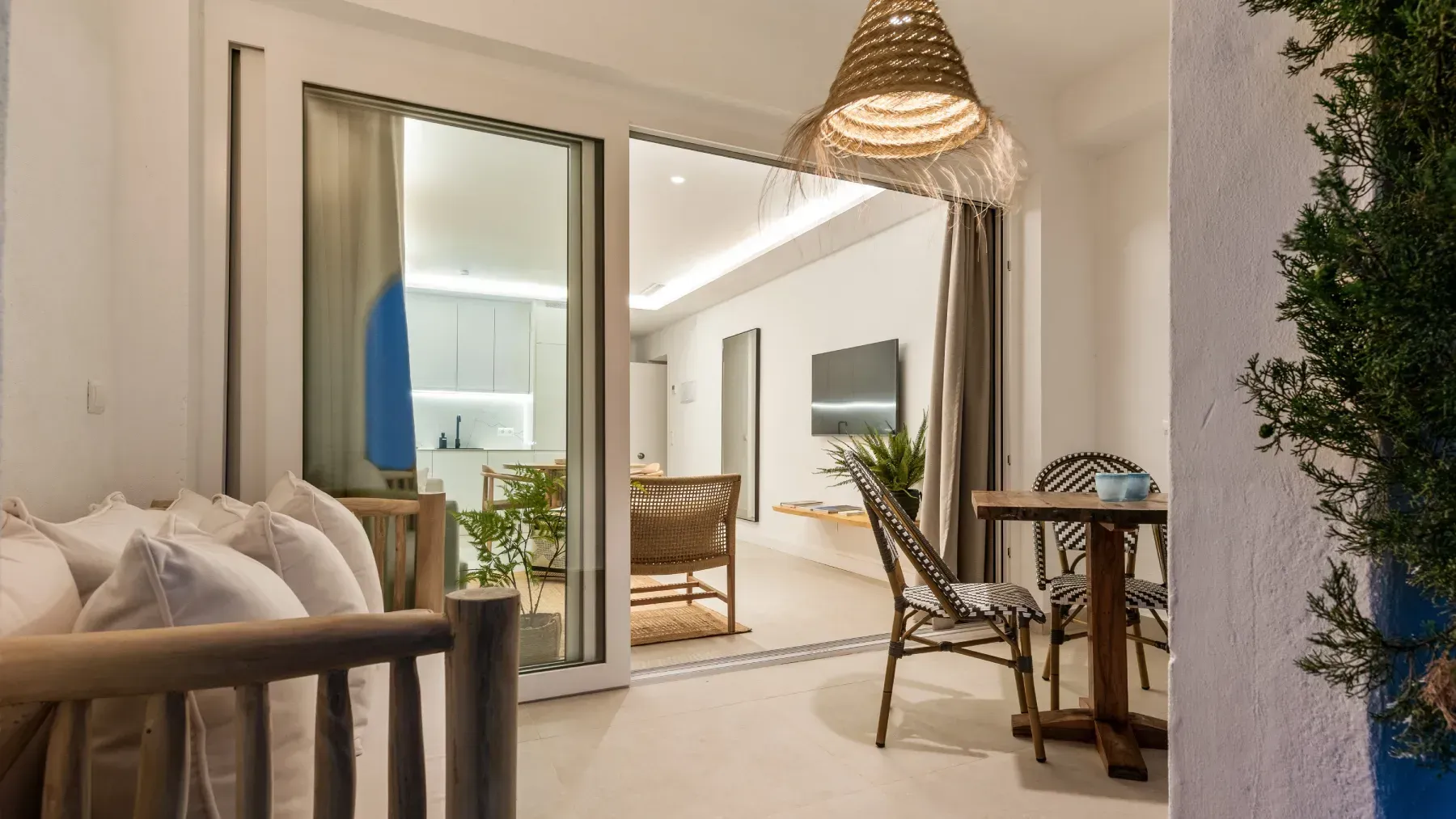 Balcón con muebles de madera con vista a un interior luminoso y moderno; colores neutros y luz natural.