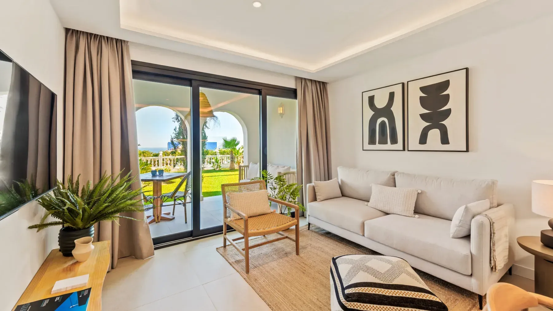 Sala de estar luminosa con colores neutros, sofá, silla, alfombra y puerta corrediza de vidrio a un patio.