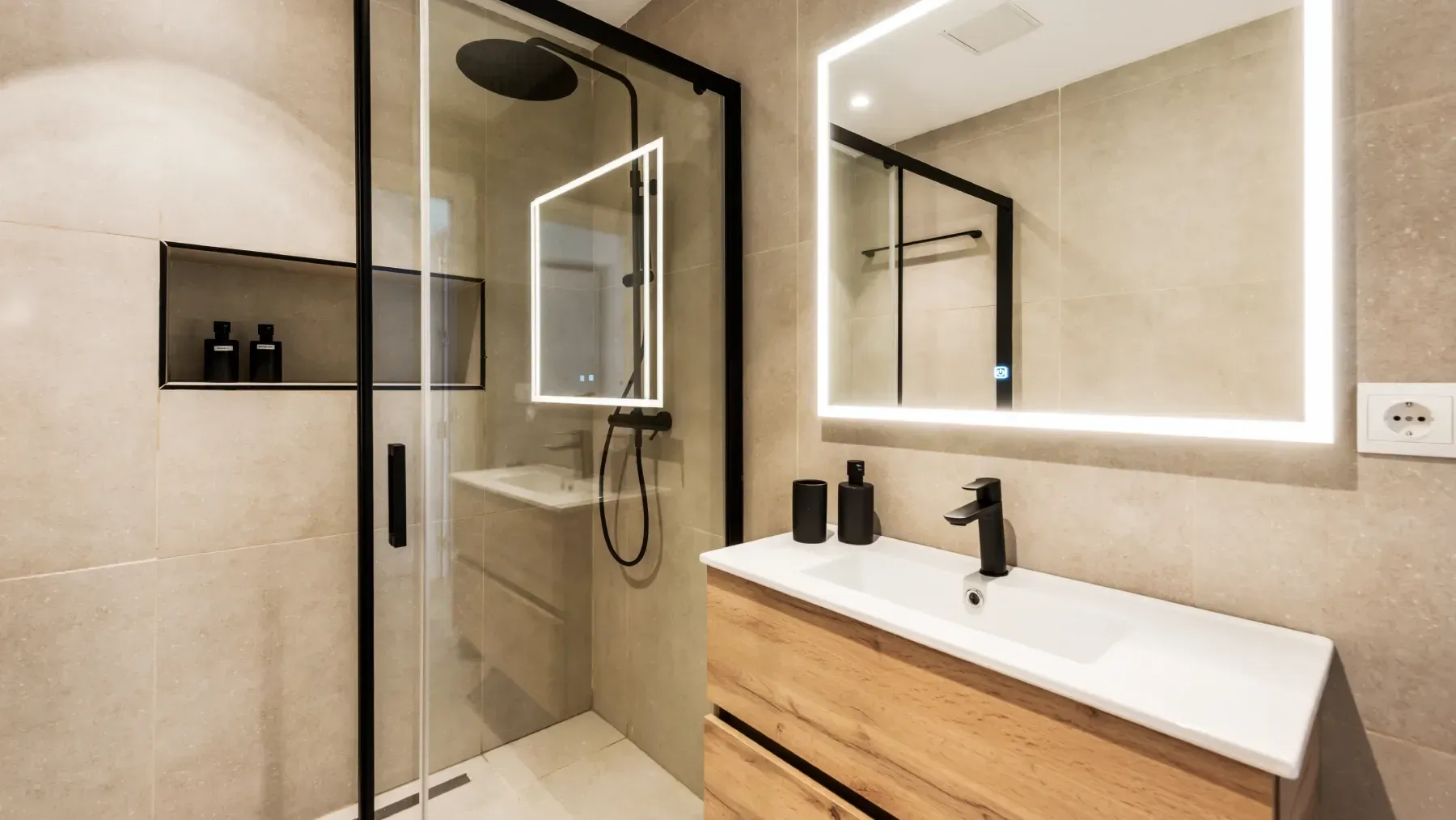 Baño moderno con ducha de cristal, tocador de madera y espejo retroiluminado.