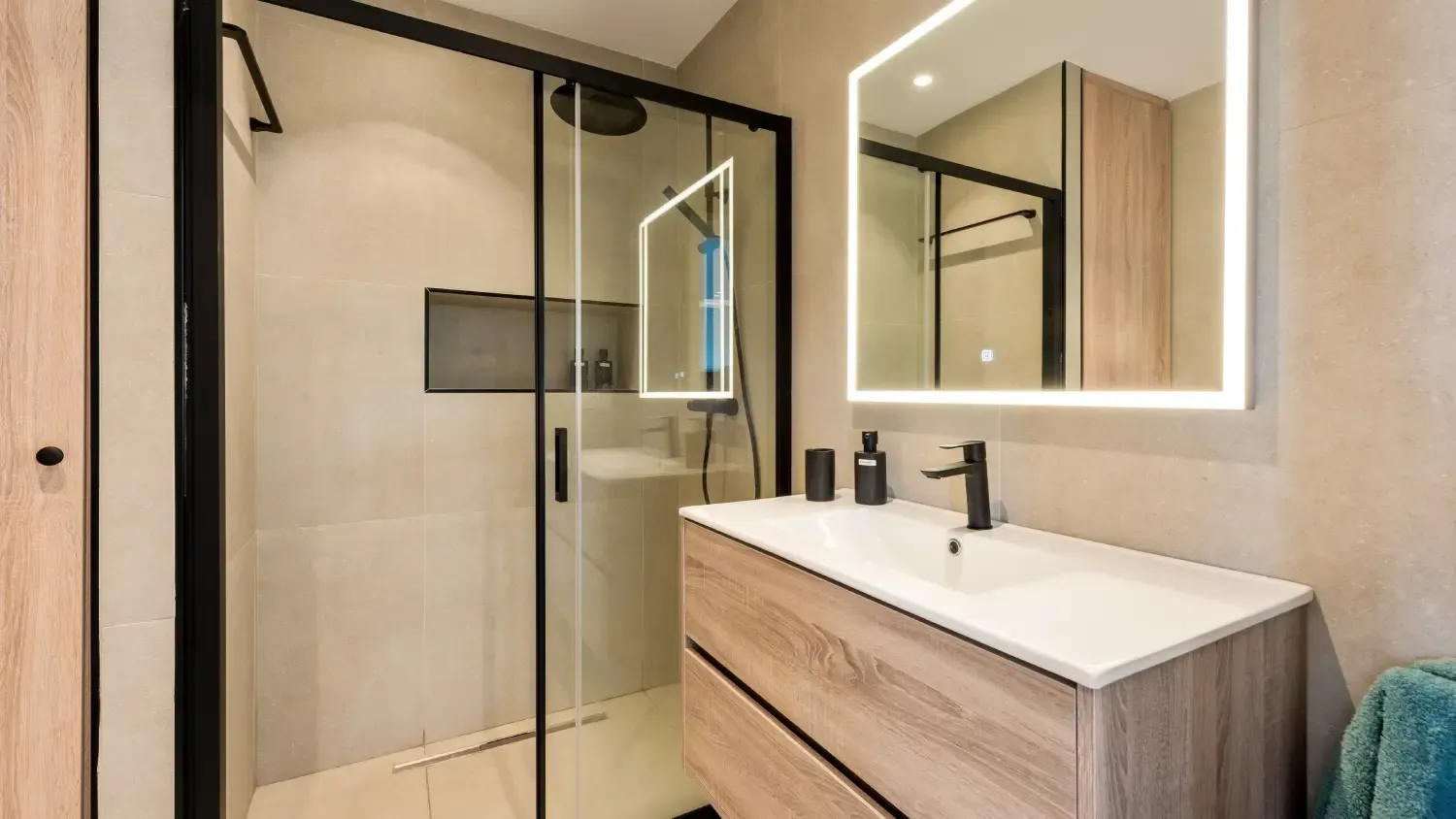 Baño moderno con tocador de madera, ducha de cristal y espejo iluminado.