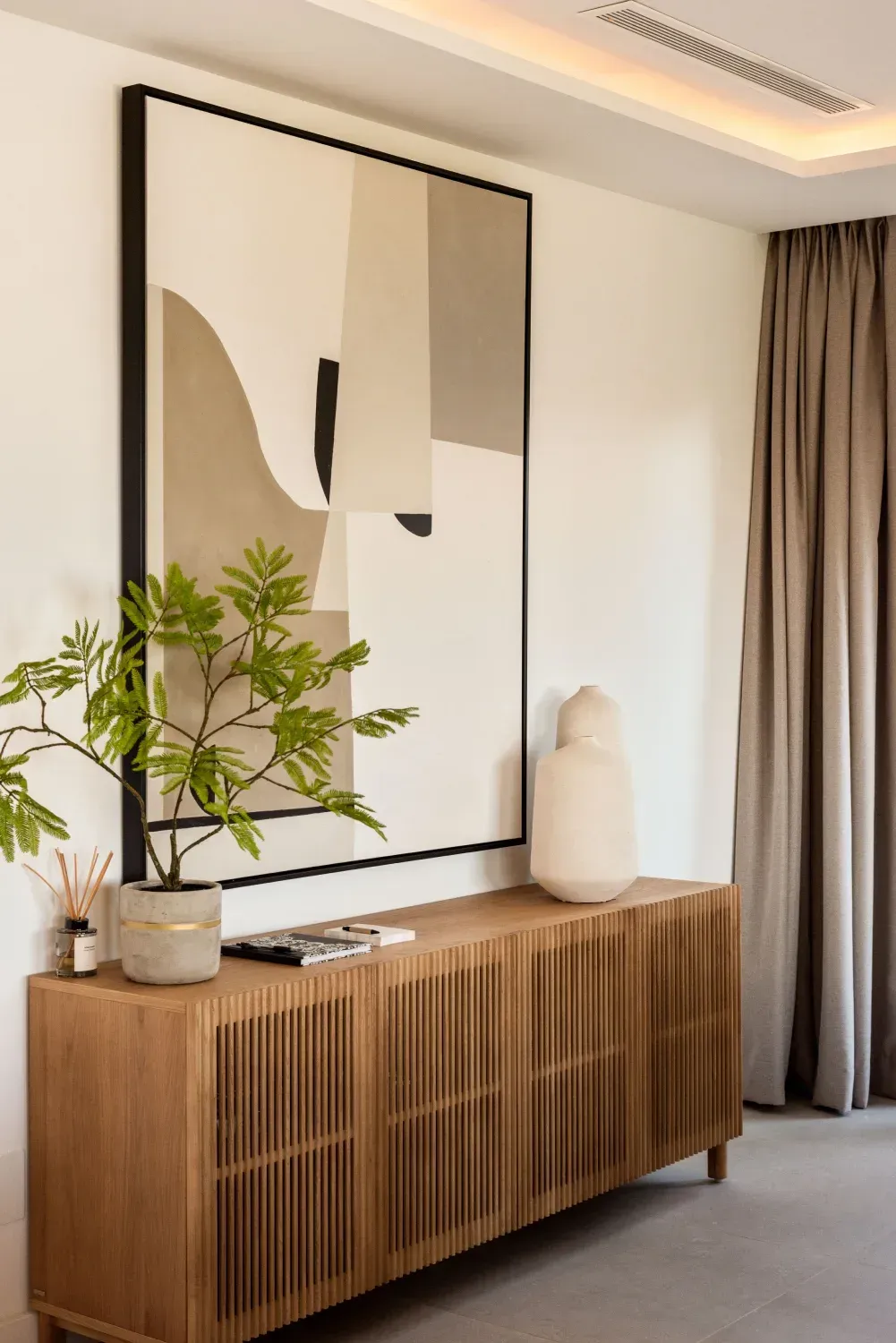 Mueble de madera con obra de arte y una planta, cerca de una cortina.