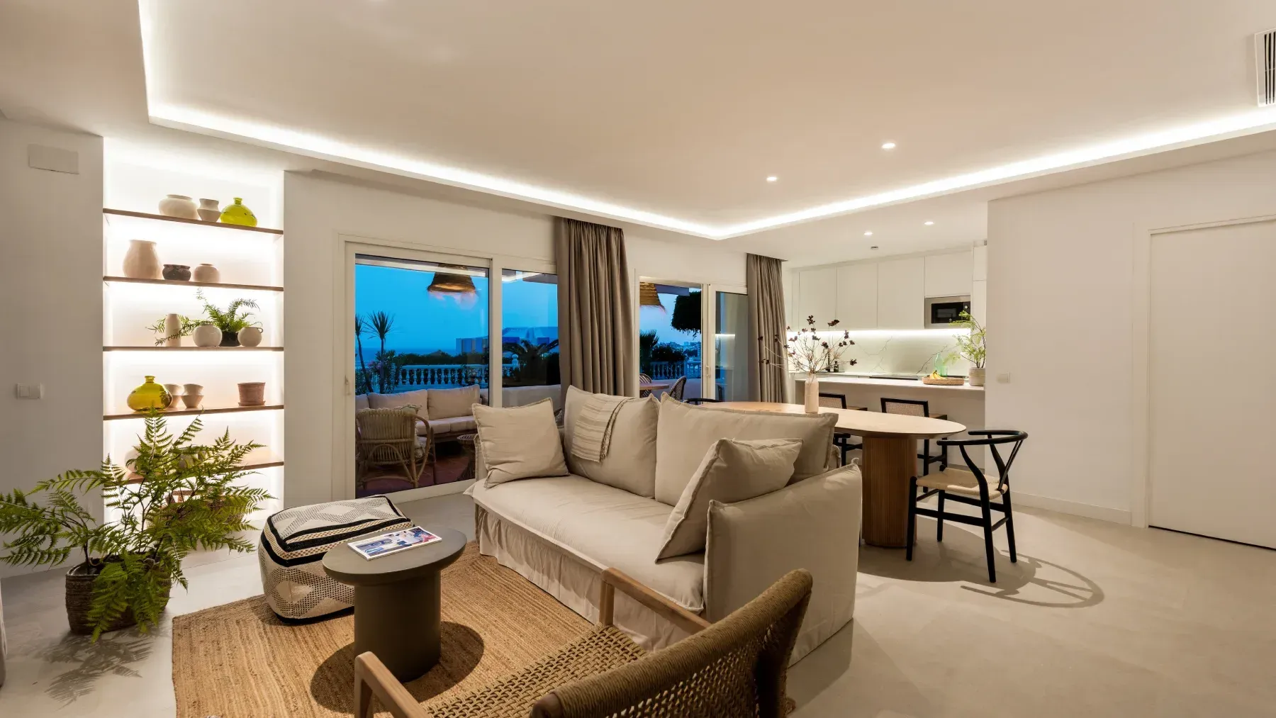 Sala de estar moderna con colores neutros, sofá y cocina abierta.