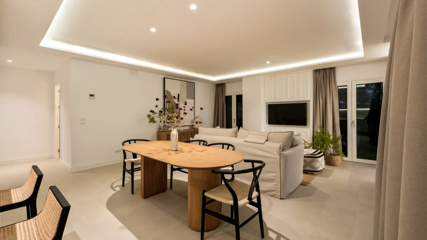 Espacio de estar de concepto abierto con comedor, sofá y televisor en una pared blanca.