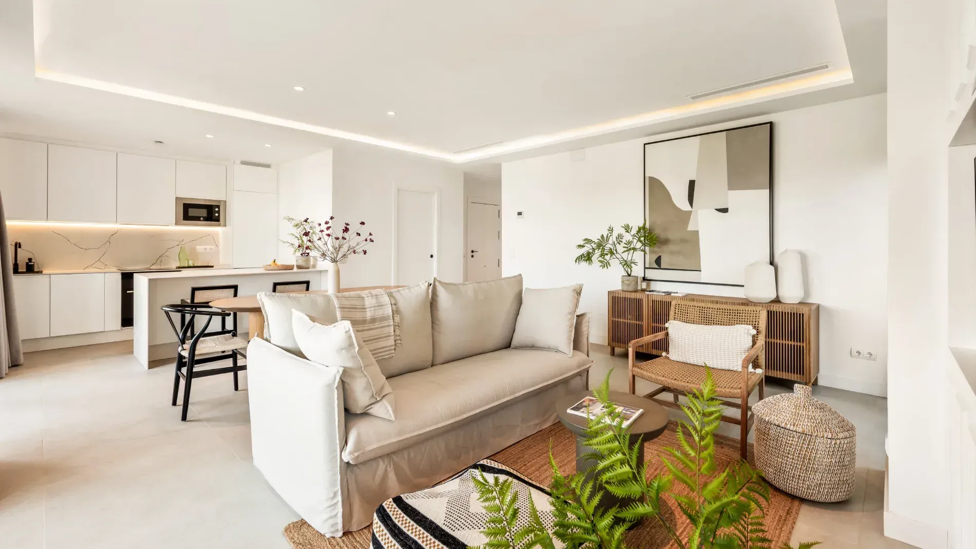 Espacio luminoso con cocina abierta, tonos neutros, muebles modernos y plantas decorativas.