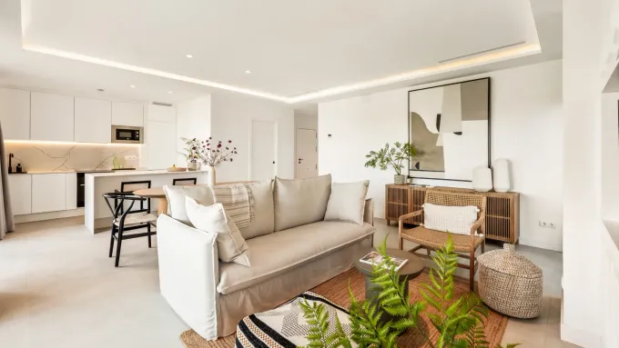 Espacio luminoso con cocina abierta, tonos neutros, muebles modernos y plantas decorativas.