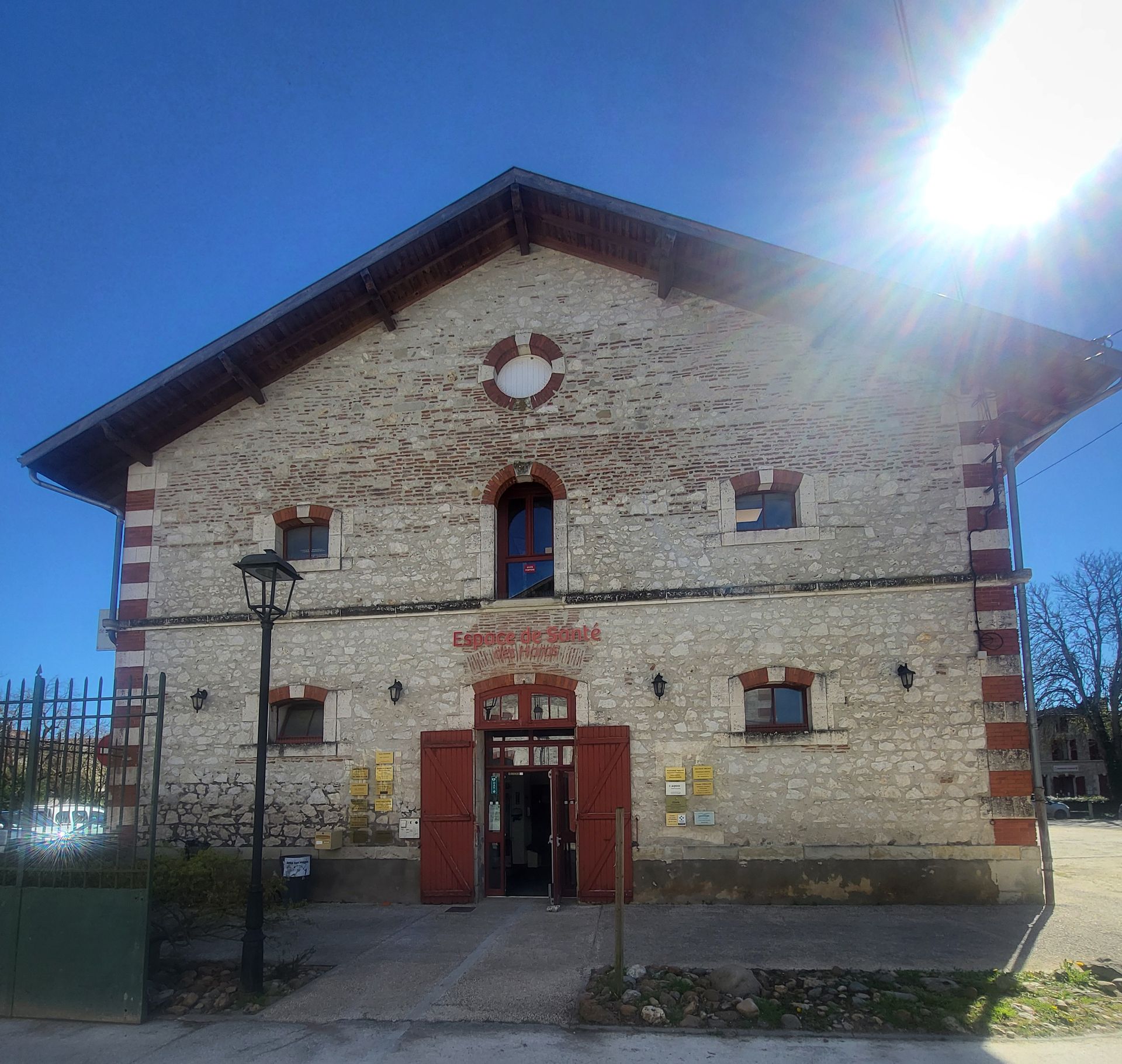 Bâtiment en pierre avec des accents de briques rouges et un toit à pignon, comportant une entrée centrale et un lampadaire au premier plan.
