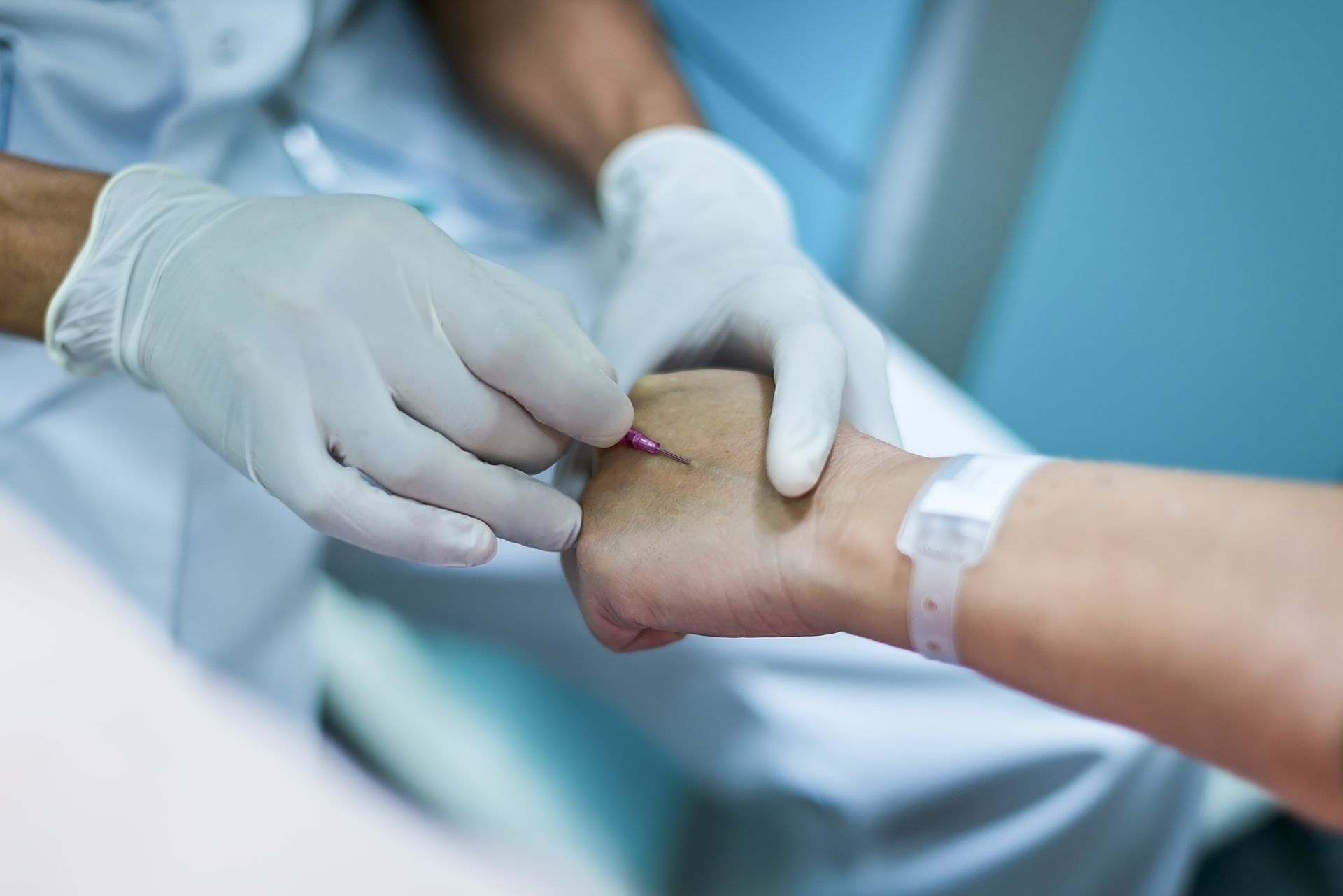 Un professionnel de santé portant des gants blancs s'apprête à insérer une aiguille dans la main d'un patient.
