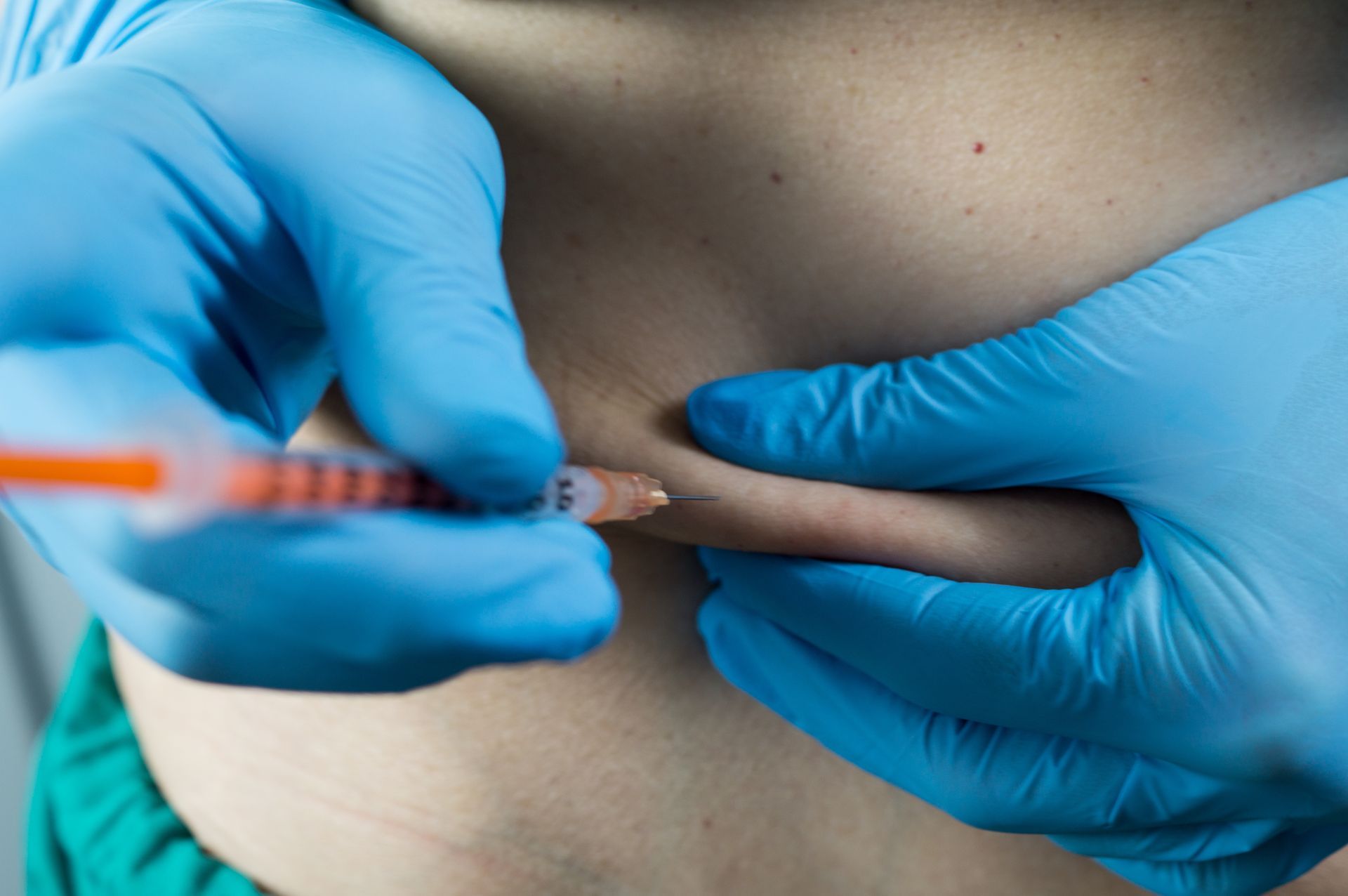 Gros plan sur des mains gantées administrant une injection sous-cutanée dans la peau de l'abdomen.