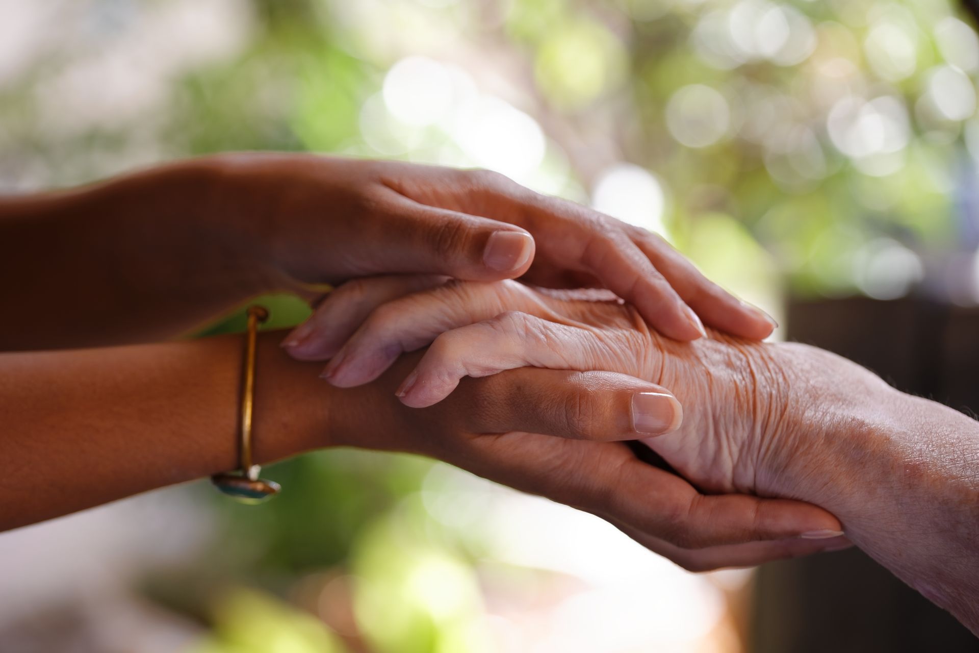 Des mains tiennent délicatement les mains ridées d'une autre, exprimant attention et connexion sur un fond doux et flou.