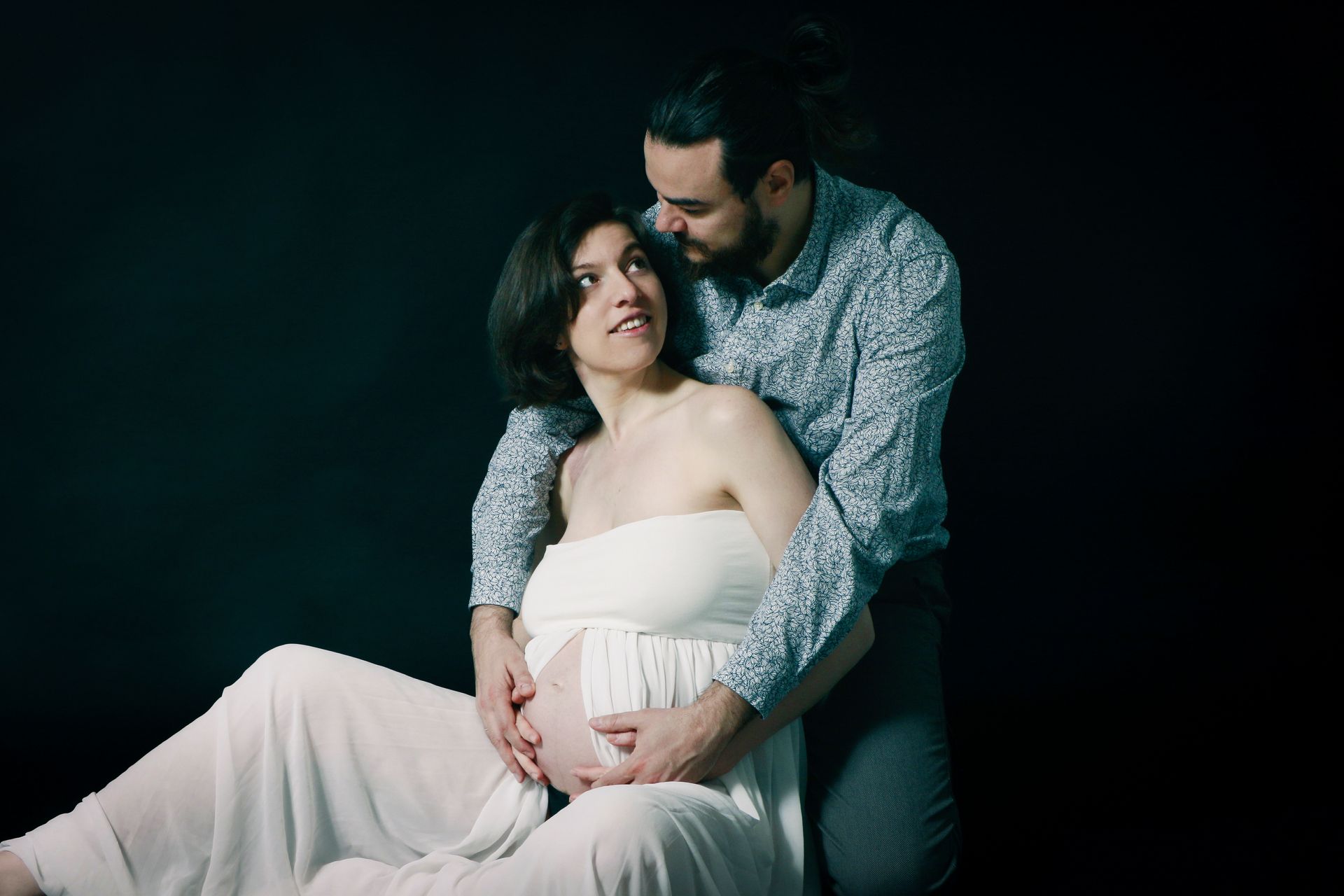 Photo d'une femme enceinte assise qui est enlacée par son conjoint