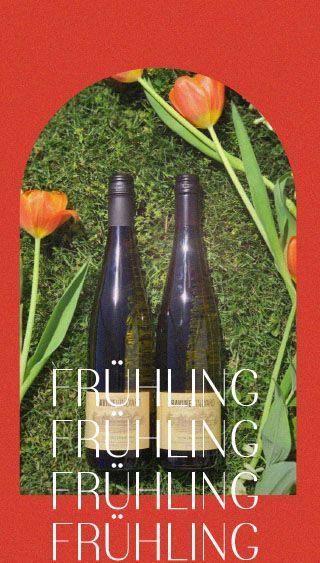 Zwei Flaschen Wein stehen auf einem üppigen grünen Feld, umgeben von Blumen.