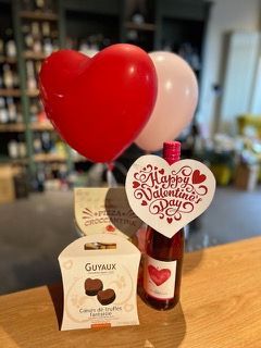 Eine Flasche Wein, eine Schachtel Pralinen und Luftballons auf einem Tisch zum Valentinstag.