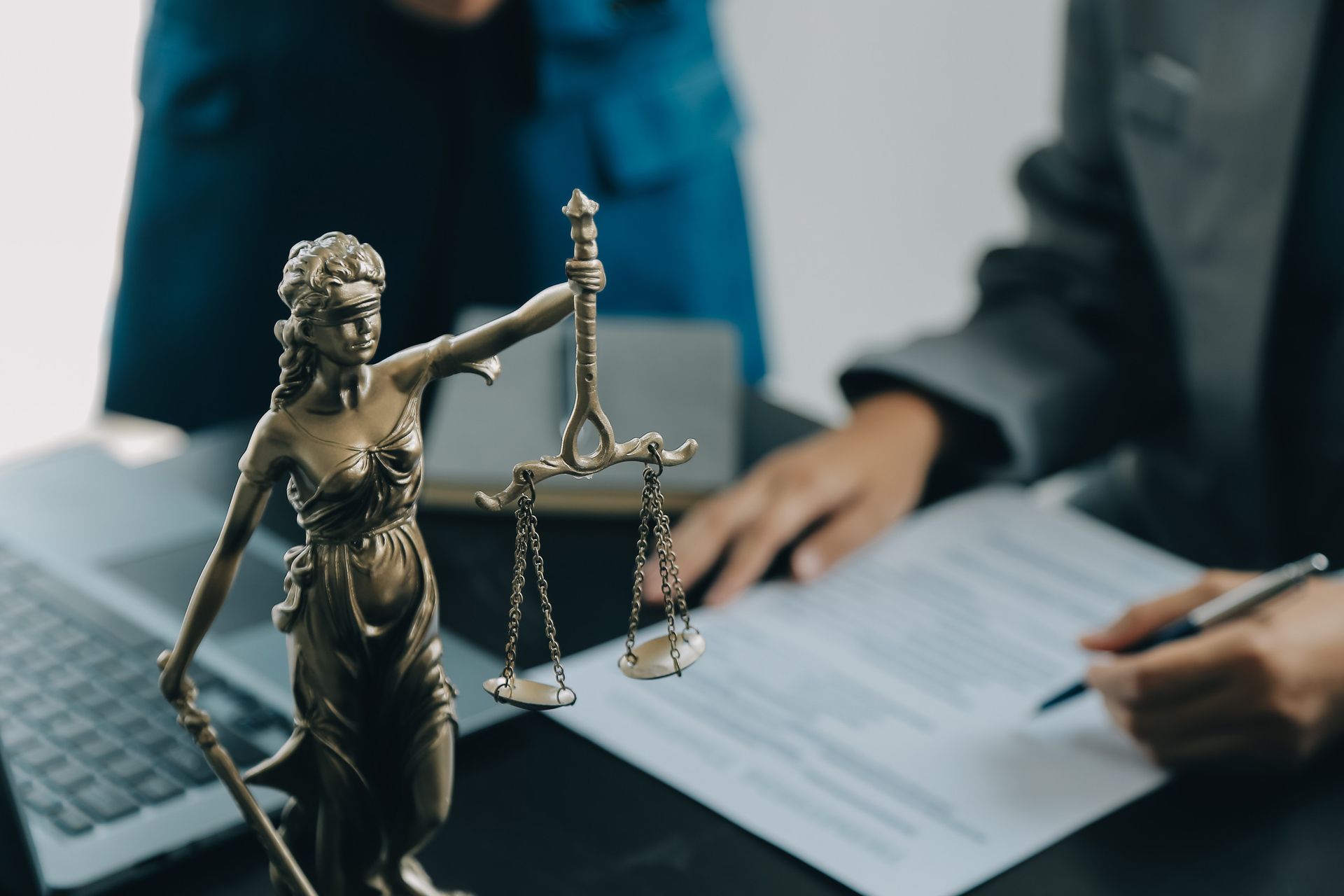 Una estatua de la Dama de la Justicia está sentada en un escritorio al lado de una persona que firma un documento.