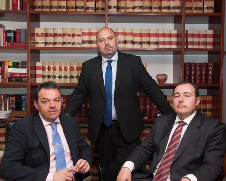 Tres hombres con traje y corbata posan frente a una estantería.