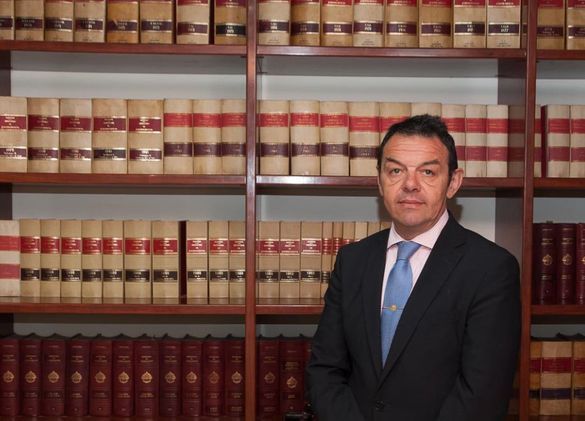 Un hombre con traje y corbata está parado frente a una estantería llena de libros.