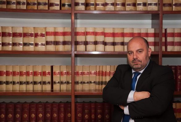 Un hombre con traje y corbata está parado frente a una estantería llena de libros.