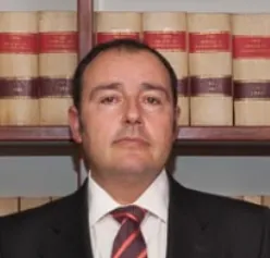 Un hombre con traje y corbata está de pie frente a una estantería.