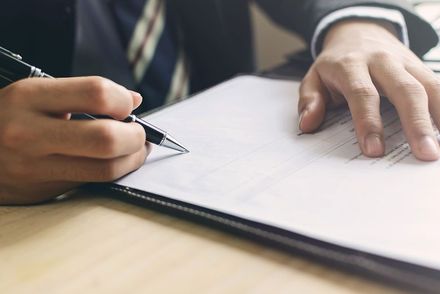 Eine Person schreibt mit einem Stift auf ein Blatt Papier.