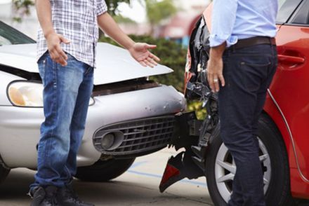 Zwei Männer stehen neben einem Auto, das bei einem Unfall beschädigt wurde