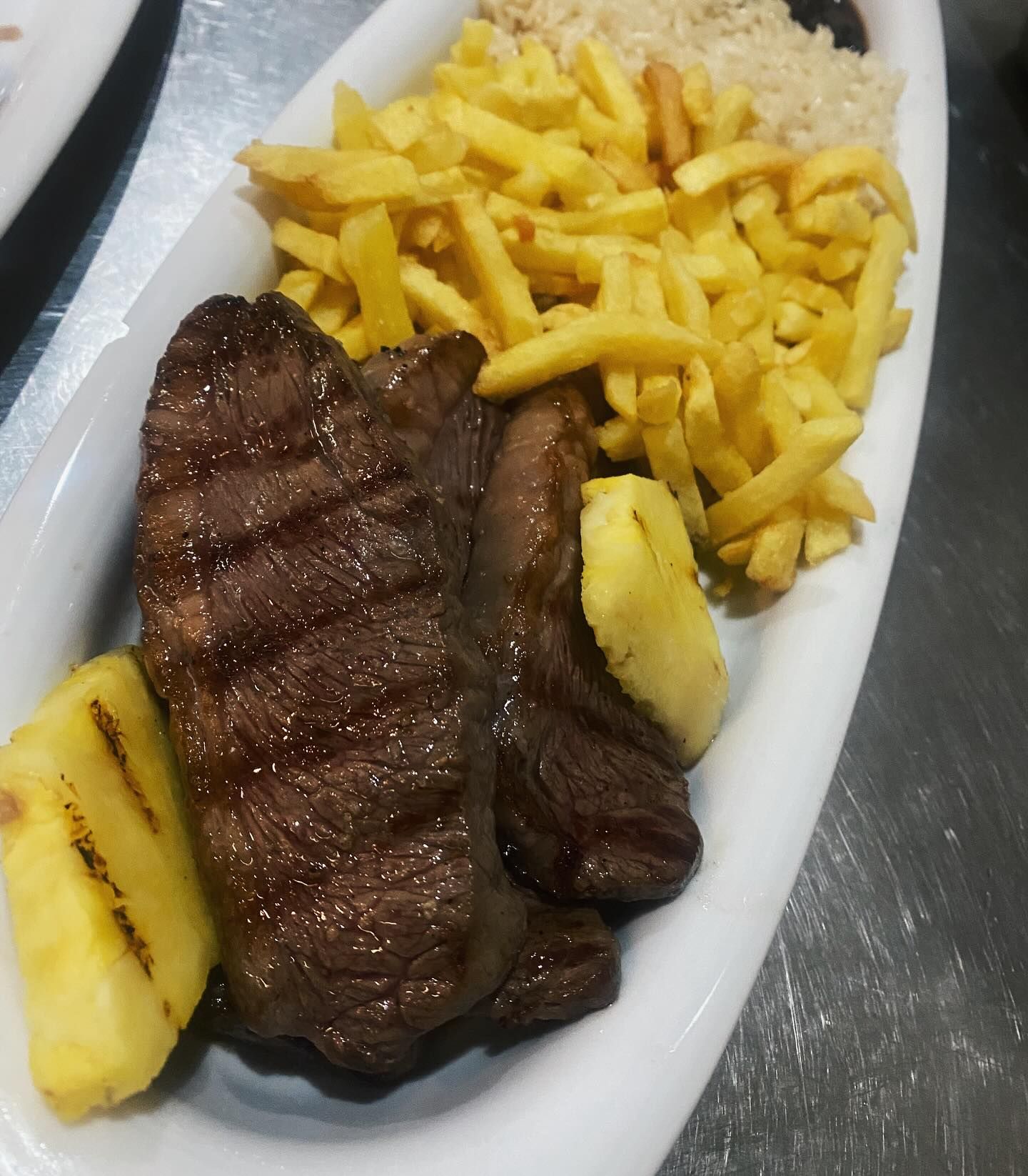 Um prato branco coberto com bife, batatas fritas e abacaxi