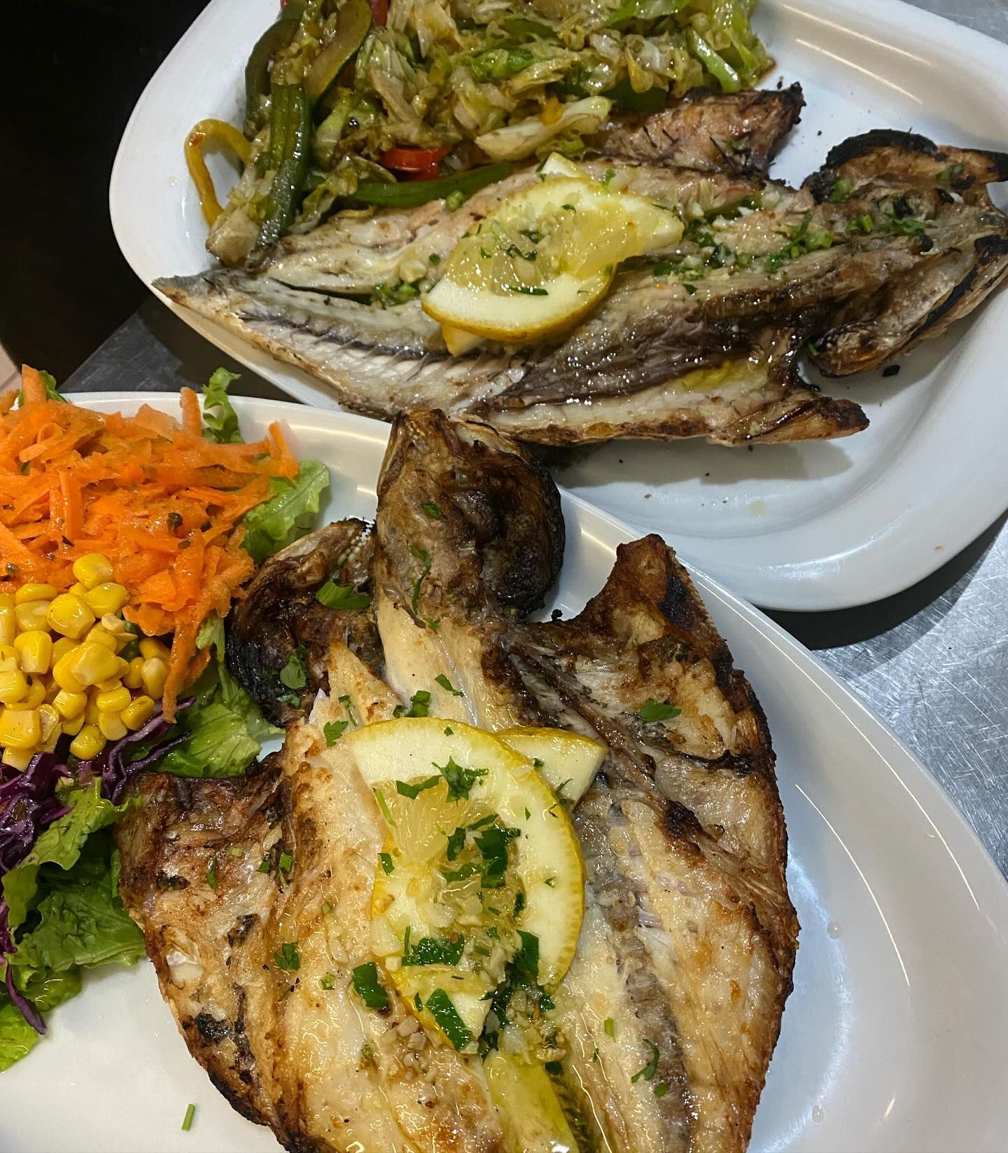 Dois pratos de comida em uma mesa, incluindo peixe e vegetais