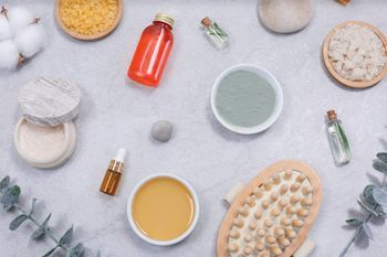 Productos de spa dispuestos sobre una superficie gris, incluidos aceites, sales, botellas, cepillos y algodón.
