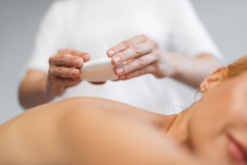 Terapeuta sostiene una piedra lisa sobre la espalda desnuda de una persona durante un masaje, con las manos cerca.