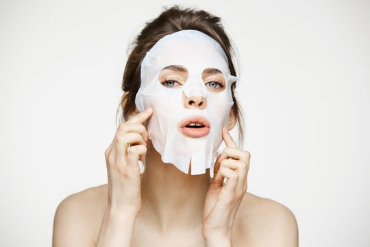 Mujer que lleva una mascarilla blanca, sosteniéndola con los dedos, sobre un fondo blanco.