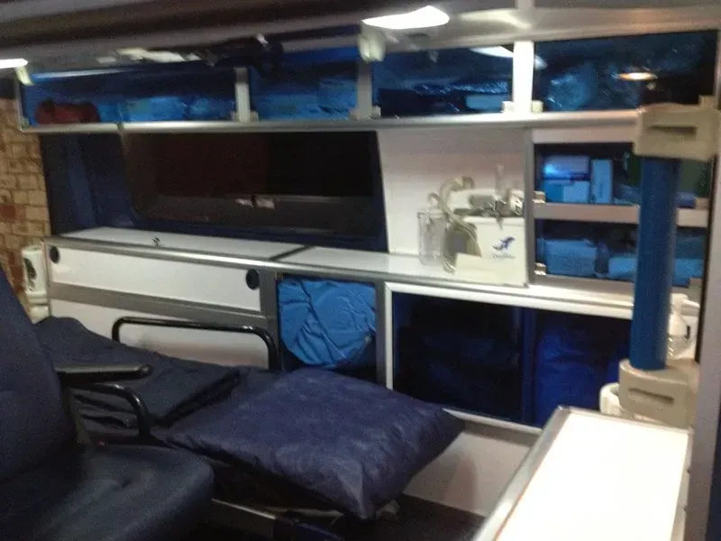 Intérieur d'une ambulance avec des fournitures médicales dans des armoires, une civière et du matériel médical.
