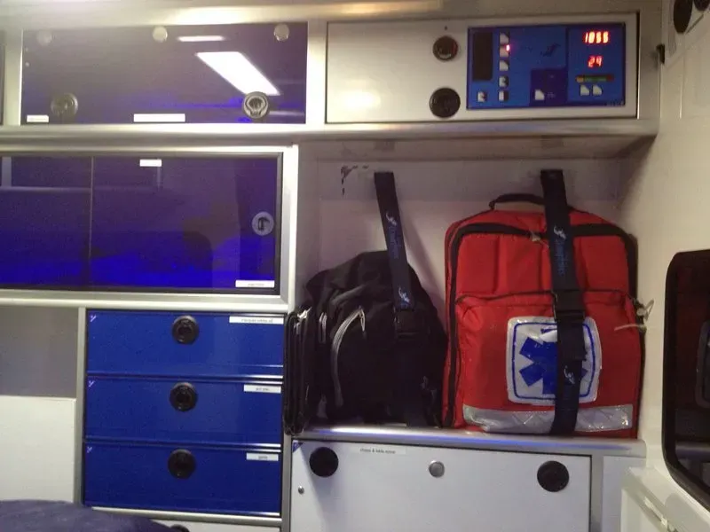 Intérieur d'une ambulance avec des armoires bleues et blanches, des sacs médicaux.