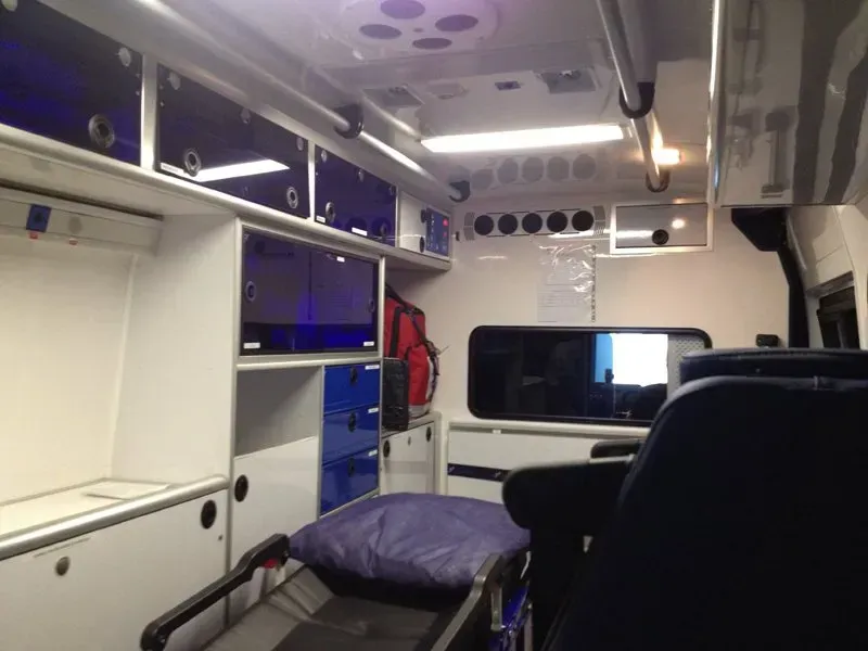 Intérieur d'une ambulance avec armoires, brancard et sièges. Couleurs dominantes : blanc et bleu.
