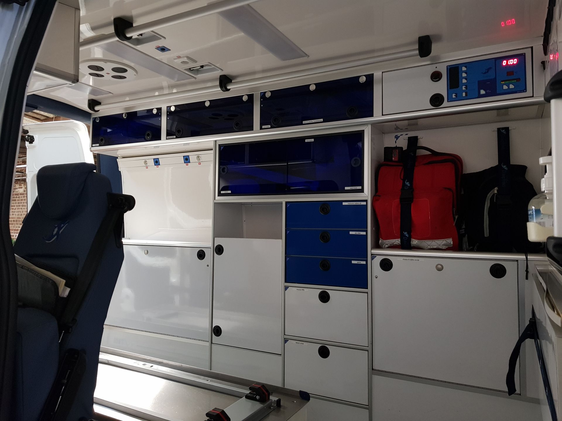 Intérieur d'une ambulance avec armoires blanches, touches de bleu, matériel médical.