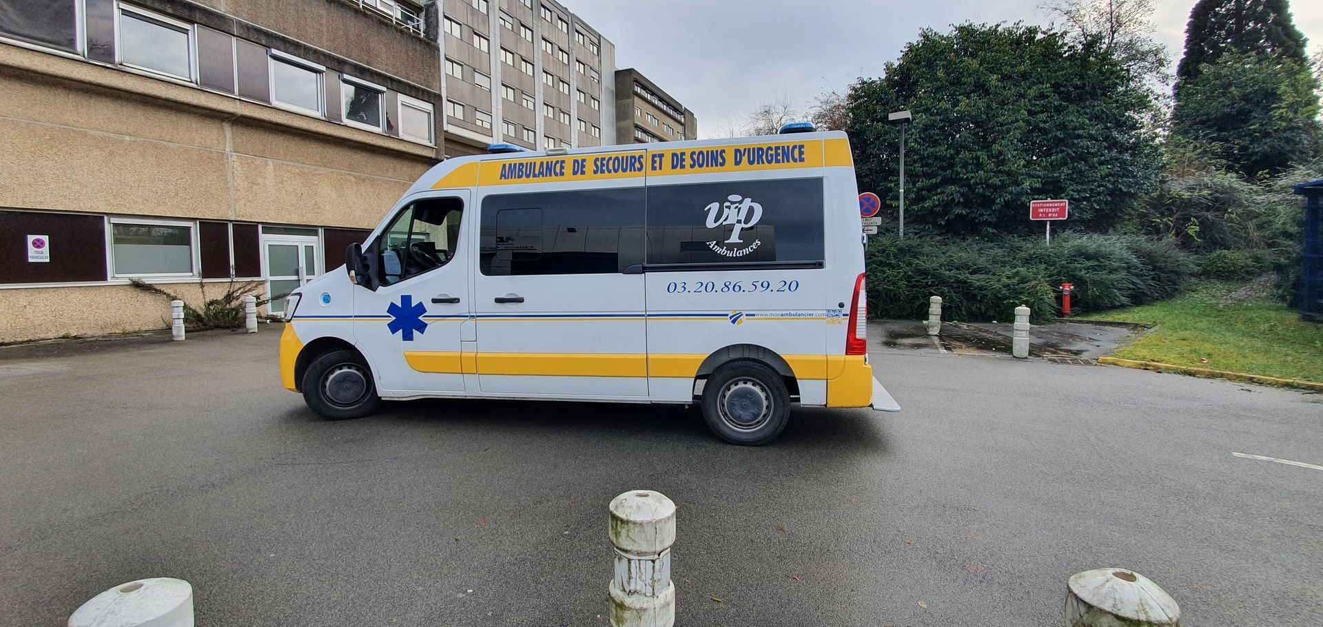 Une ambulance blanche avec des touches de jaune est garée près d'un bâtiment.