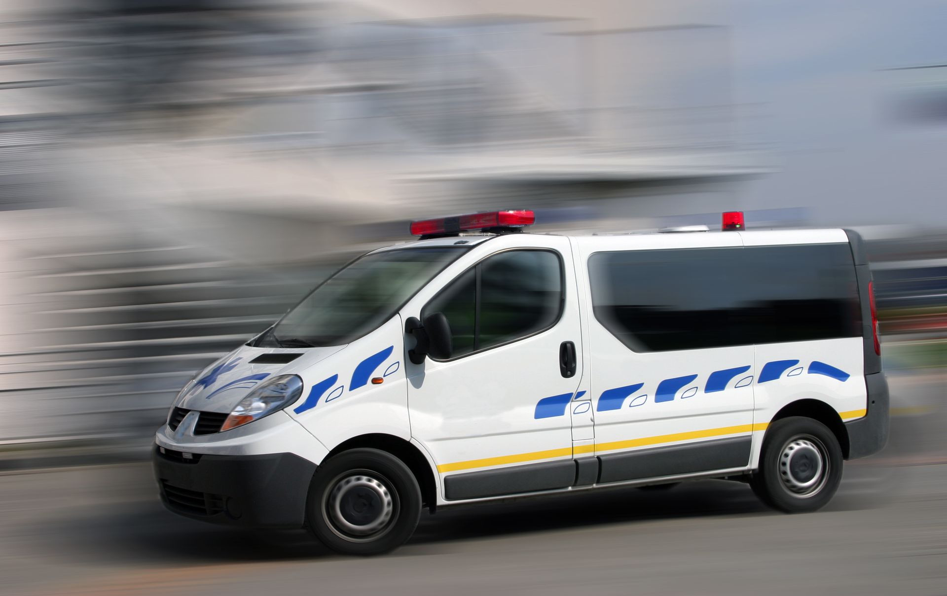 Fourgon de sécurité blanc et bleu avec gyrophares rouges clignotants, mouvement flou.